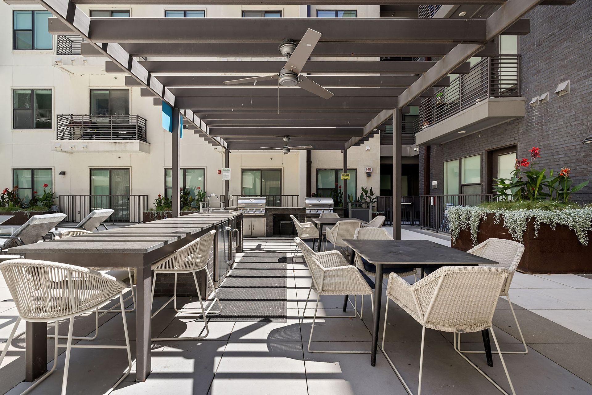Outdoor patio dining area with tables, woven chairs, and a pergola in bright sunlight
