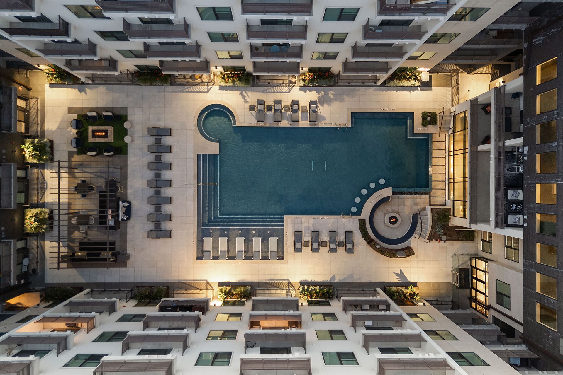 Overhead view of a hotel courtyard with a blue swimming pool, lounge chairs, and surrounding buildings
