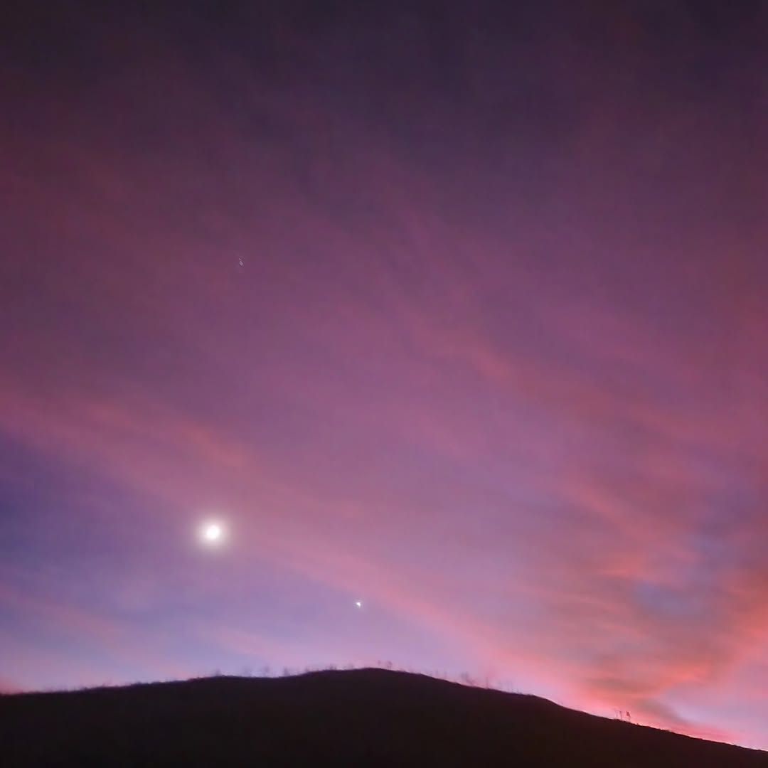 Pink-purple twilight sky over a dark hill silhouette, with a bright moon or planet near the horizon.