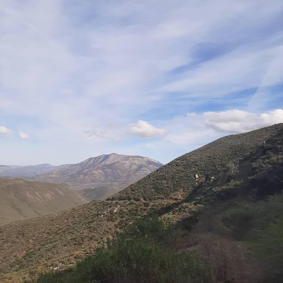 Mountain valley landscape with rocky hills, green slopes, and a partly cloudy blue sky