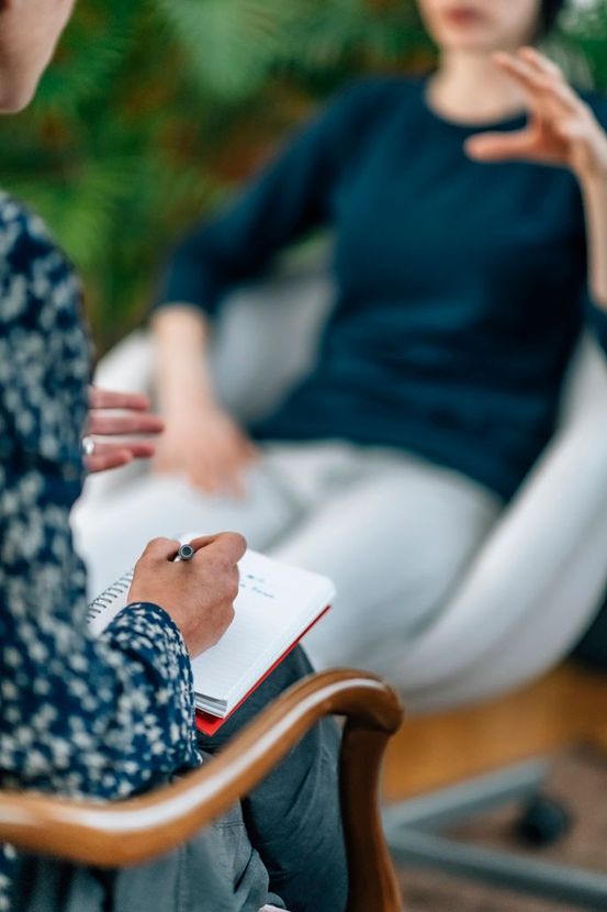 Person writing notes during a seated conversation in a blurred indoor setting