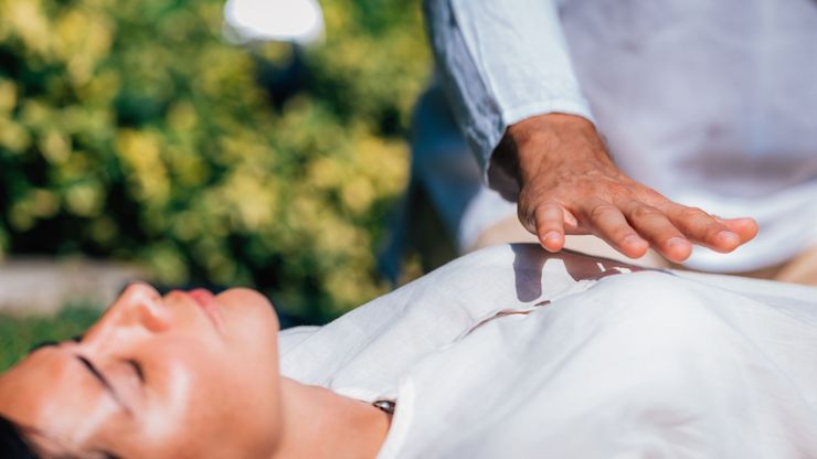 Hand hovering over a person lying down outdoors, suggesting a healing or reiki session