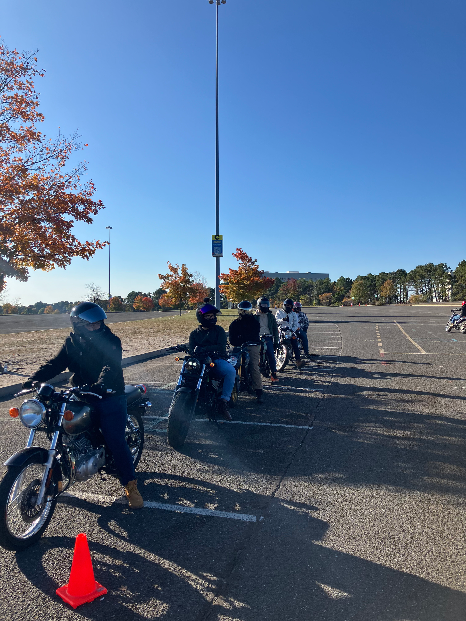 A woman is riding a motorcycle in a parking lot next to traffic cones.