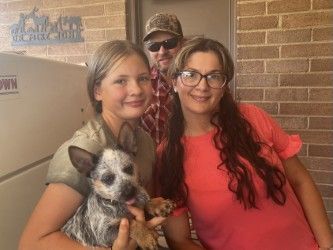 Two women posing with a small dog indoors, with a man standing behind them.