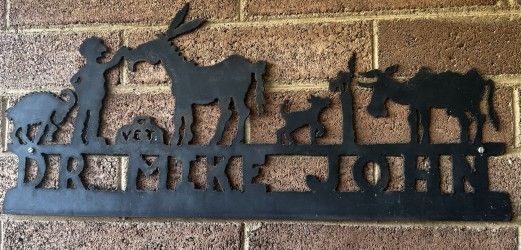 Black metal farm sign with silhouettes of a horse, deer, dog, bird, and goats against a brick wall