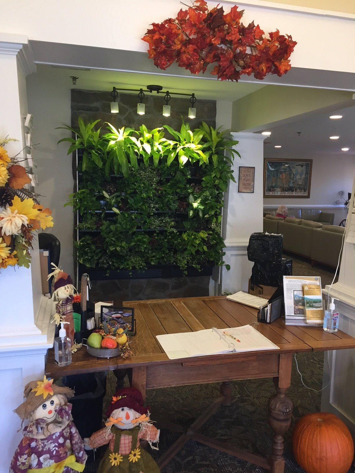 Lobby with a green plant wall, wooden table, and autumn decorations, including pumpkins and scarecrows.