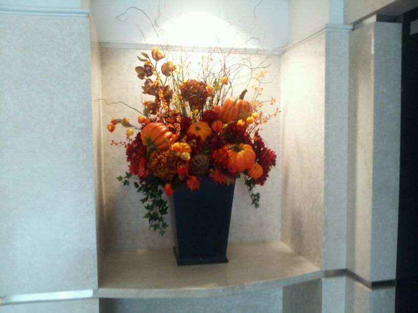 Tall black vase with orange and red autumn flowers in a wall niche