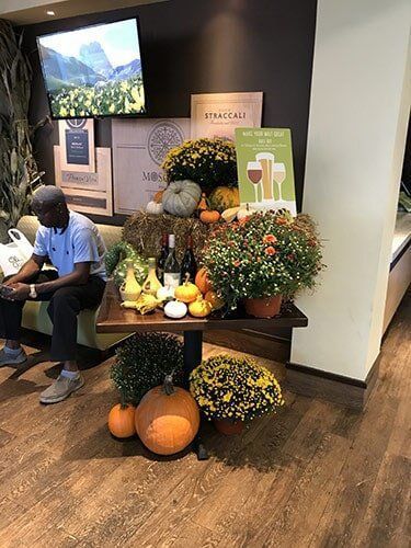 Person seated beside a fall display of pumpkins, gourds, and flowers in a store lobby.