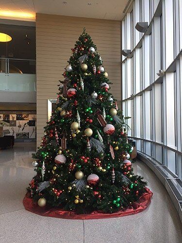 Decorated Christmas tree with red, gold, and white ornaments in a lobby by large windows