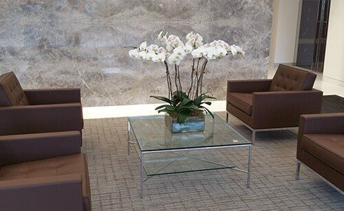 Lobby seating area with brown chairs and a glass coffee table holding white orchids