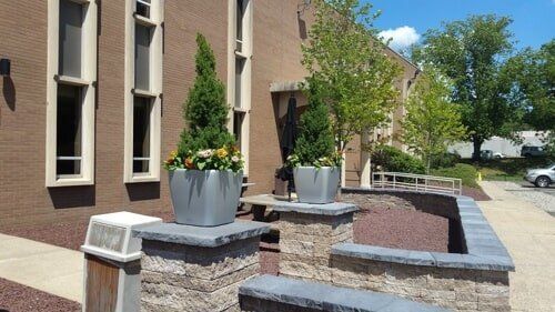Landscaped building entrance with stone planters, beige brick walls, and blue sky