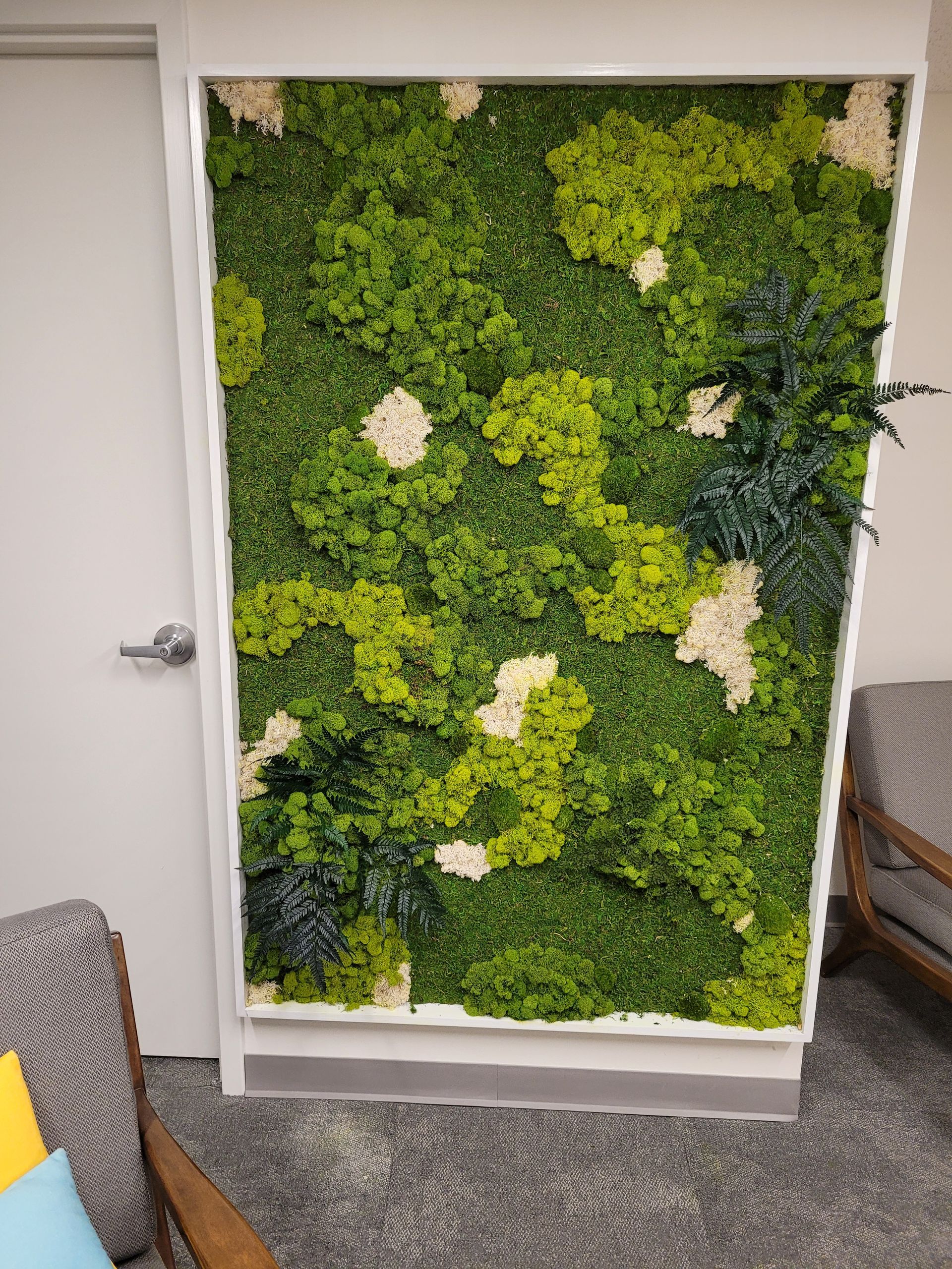Green moss wall panel with white floral accents in an office or lounge area