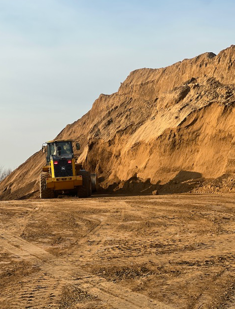 A bulldozer is driving through a dirt field in front of a large pile of dirt.