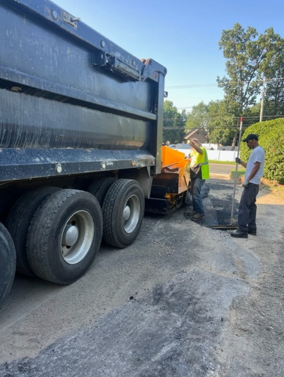 Two men are working on a road next to a dump truck.