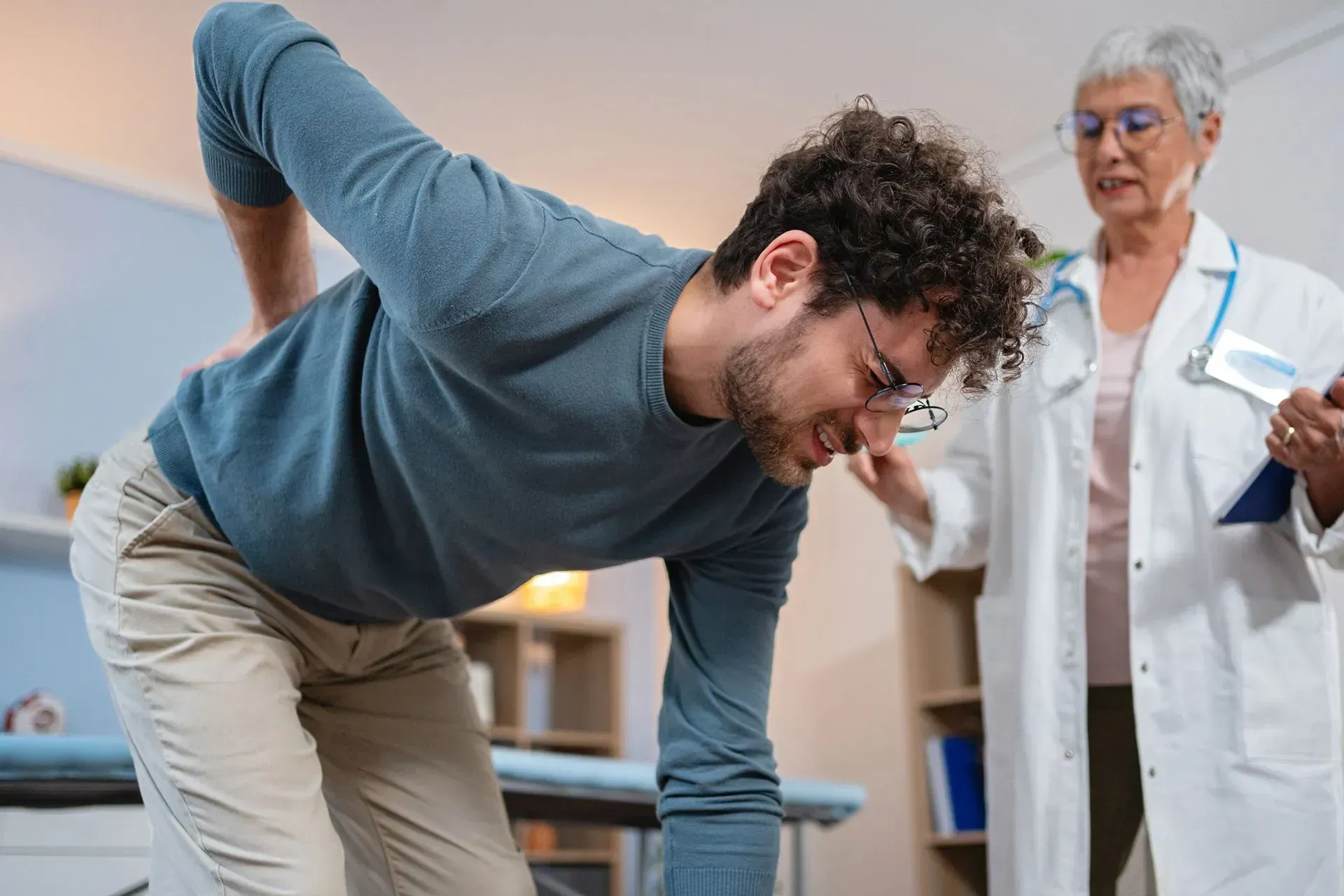 Man with back pain being examined by a doctor in an office.
