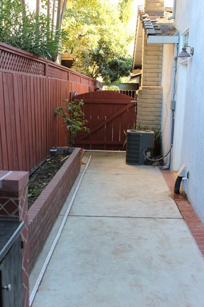 A concrete walkway leading to a house with a red fence.
