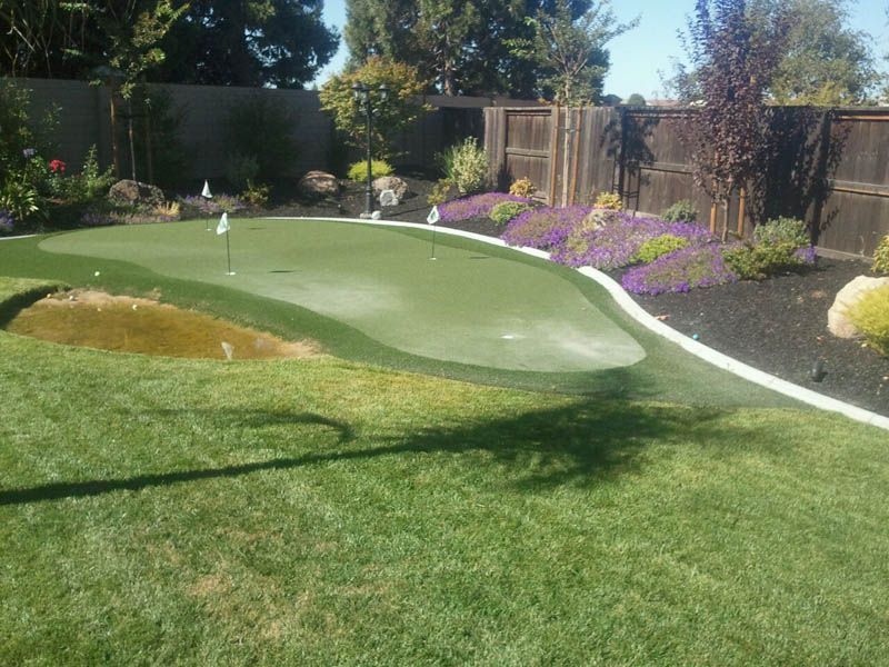 A golf course in a backyard with a pond in the middle.
