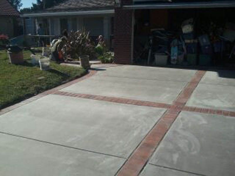 A concrete driveway with a brick border is in front of a house.