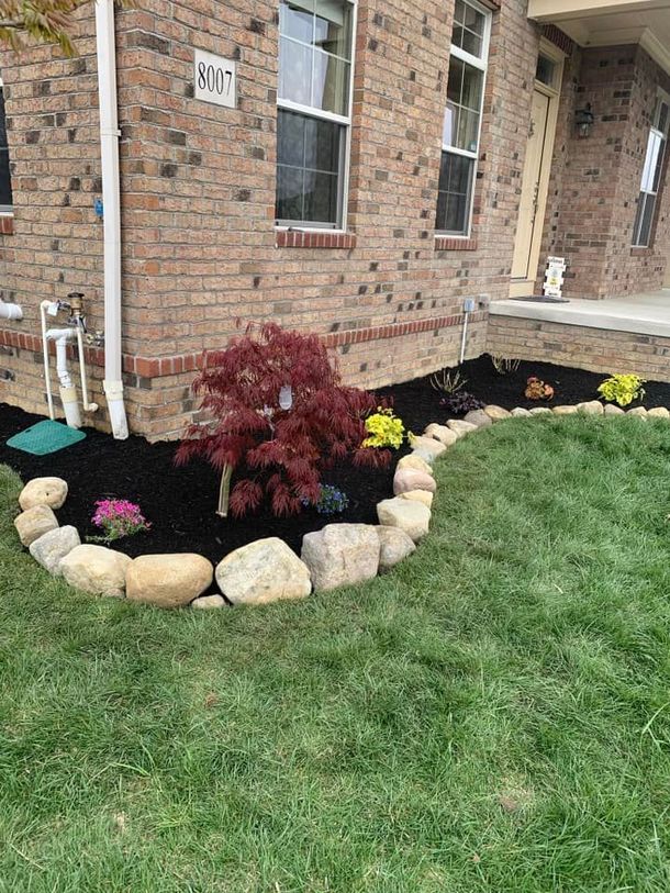 Landscaped front yard with a brick house, a red tree, and stone edging.