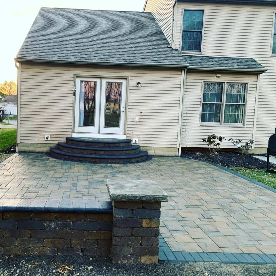 Backyard patio with brick pavers, raised steps to French doors, and a decorative wall.