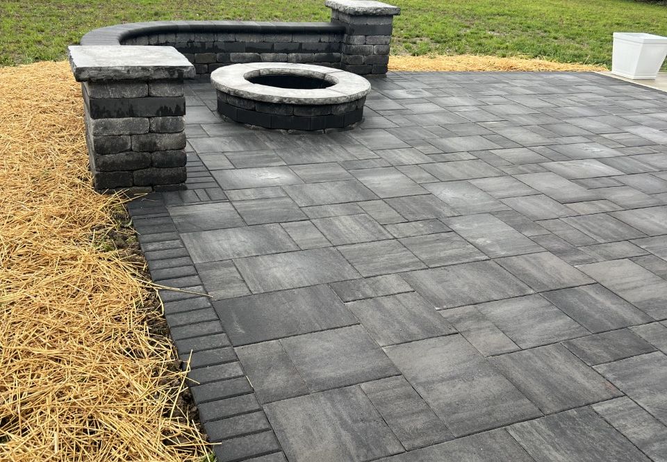 Patio with gray pavers, built-in seating, and a fire pit. Dry grass borders the patio.