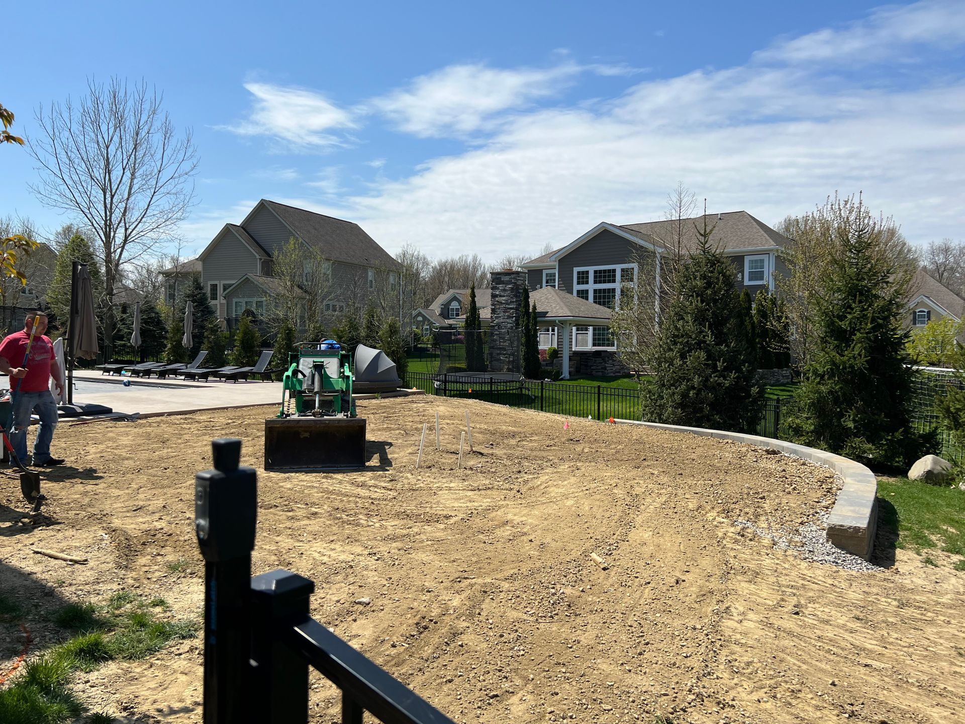 Man near a lawn, preparing the area with machinery, houses in the background. Sunny day.