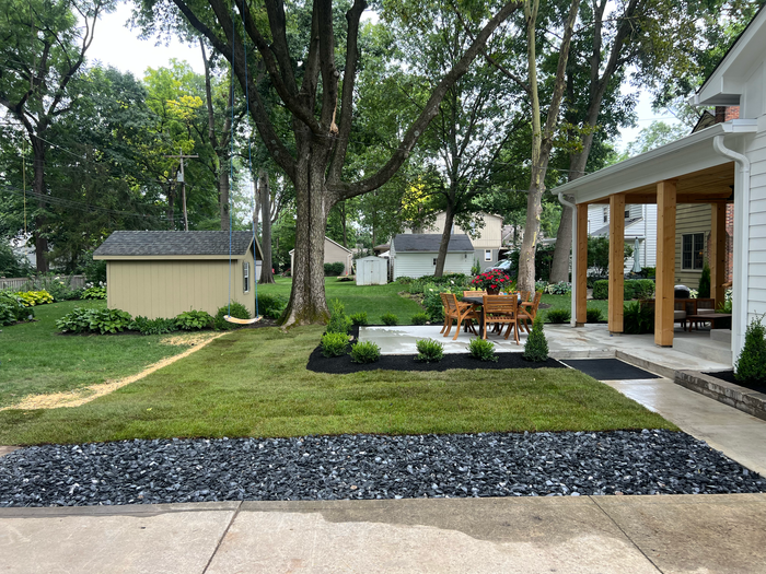 Lawn and garden with shed, patio, trees, and house. Black stone border and new sod in foreground.