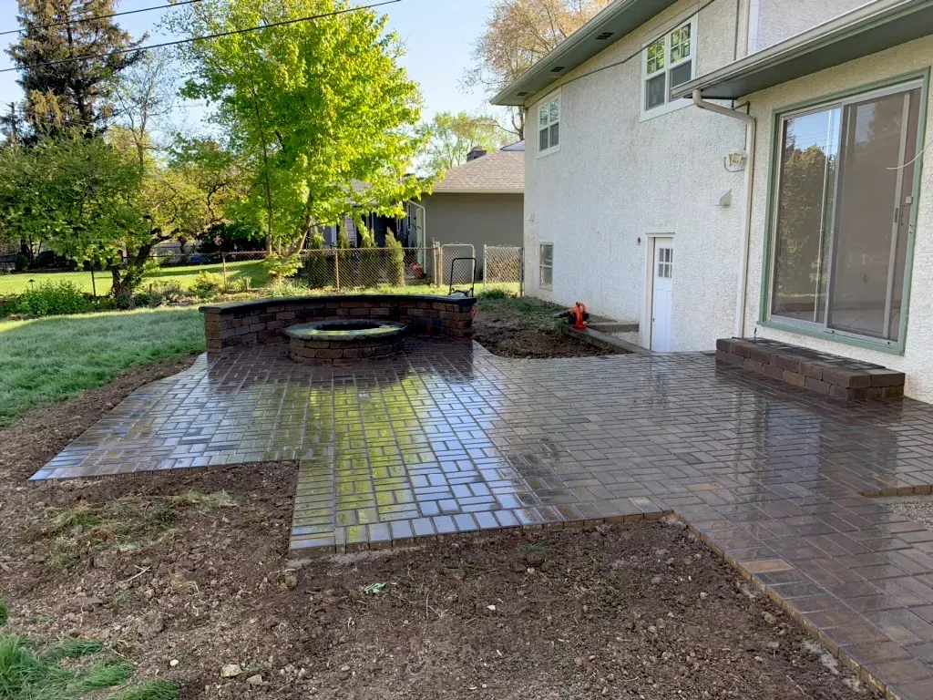 Brick patio with fire pit, adjacent to a two-story beige house with sliding glass door.