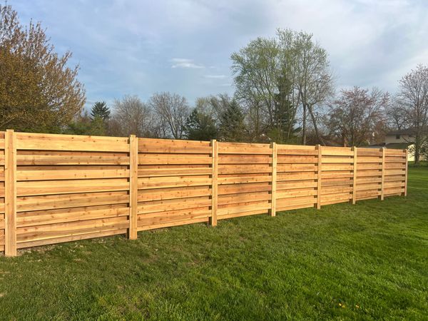 Wooden fence in a grassy yard, with trees and a blue sky in the background.