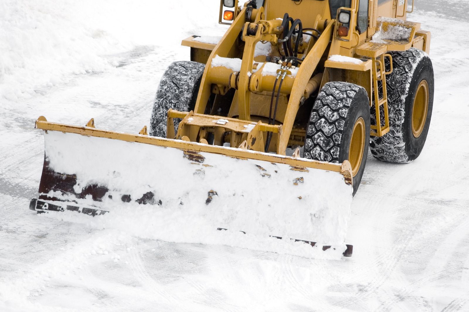 Yellow snowplow clearing snow on a white surface.