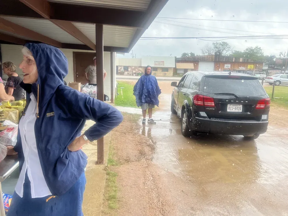 A woman in a blue jacket is standing in the rain next to a car.