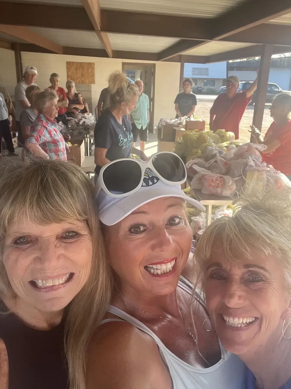 Three women are posing for a selfie in front of a crowd of people.