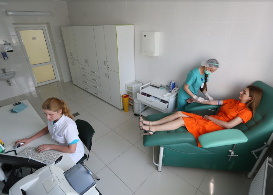 Двоє людей отримують стоматологічну допомогу в клініці, а стоматолог працює поруч із зеленими кріслами-рекламодами.