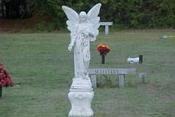 White angel statue in a cemetery with flowers and grave markers in the background