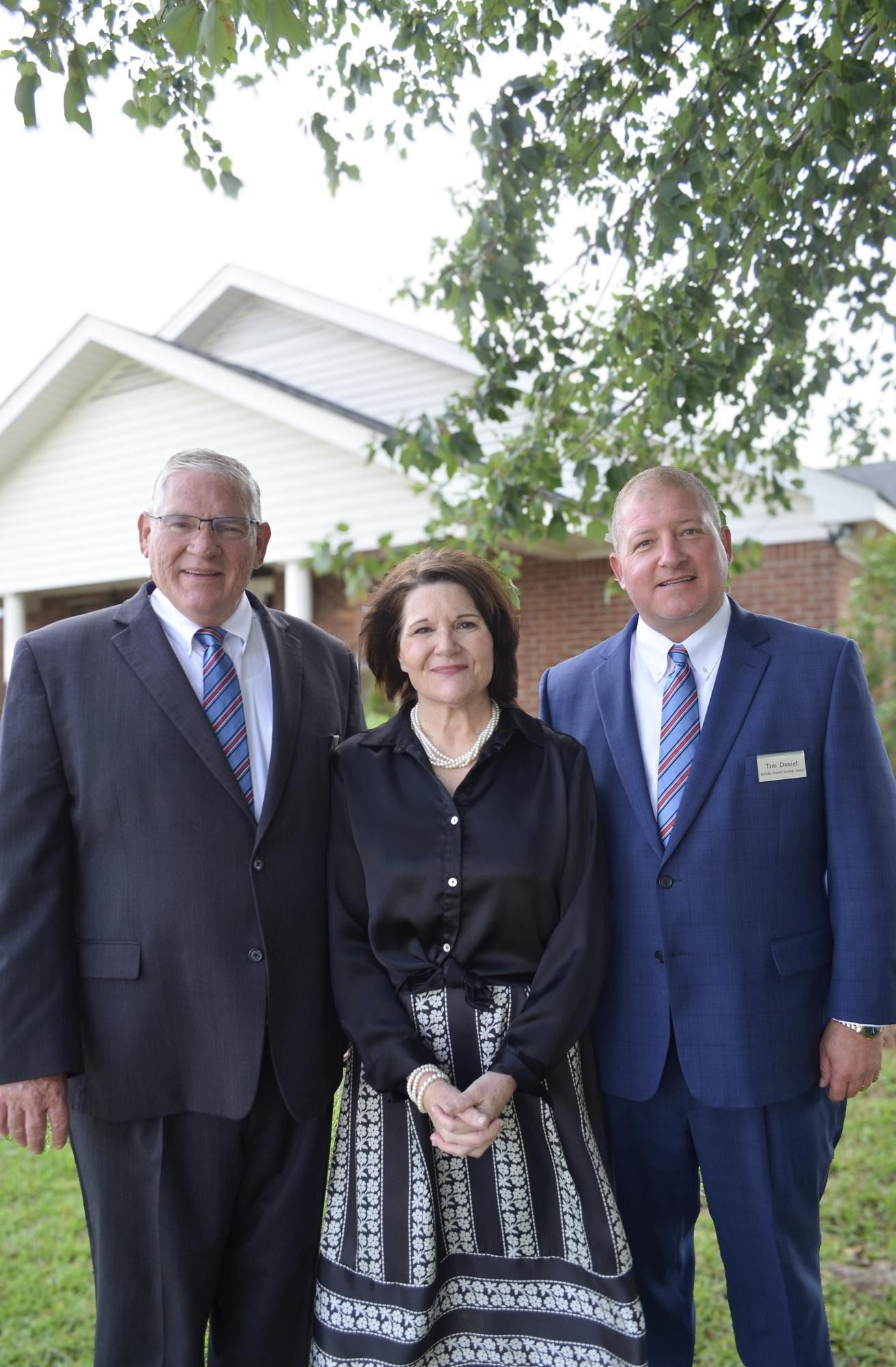 Three people standing outdoors in front of a house, posing for a photo