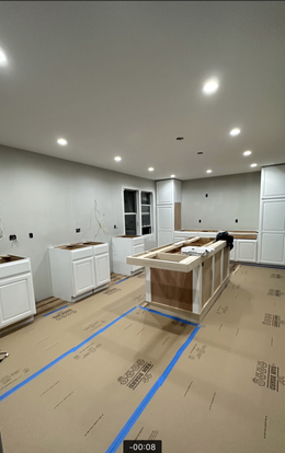 Kitchen renovation in progress: white cabinets, island with wood countertop, walls are gray, floors covered in cardboard.