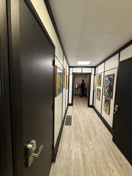 Narrow hallway with framed art on white walls, black trim, and a person at the far end.