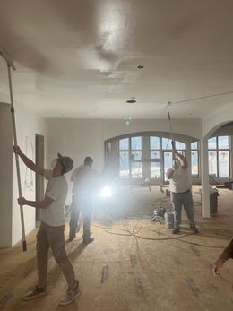 Workers smoothing a ceiling in a room with light streaming in.