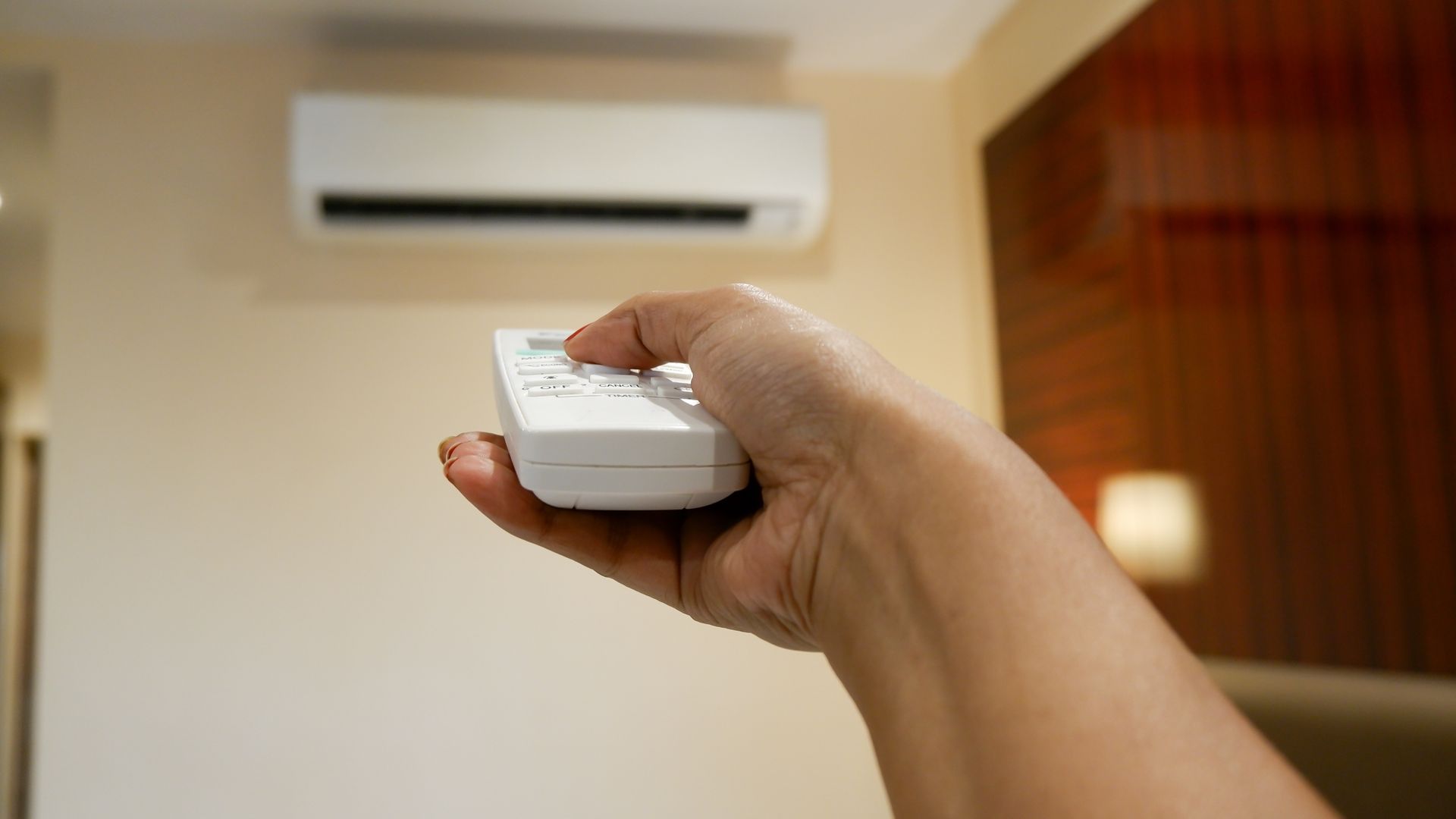 A hand points a remote control toward a wall-mounted air conditioning unit in a room. — Unger Air in South Tamworth, NSW