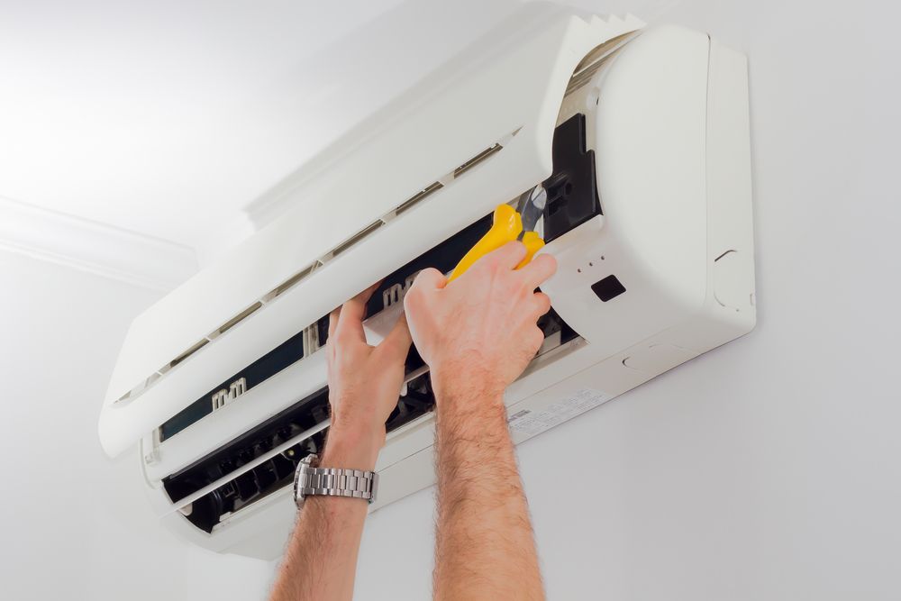 Hands repairing a white wall-mounted air conditioner unit using yellow-handled wire cutters. — Unger Air in South Tamworth, NSW