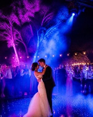 Bride and groom embracing on a dance floor under purple and blue stage lights at a nighttime wedding