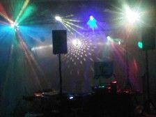 DJ setup in a dim room with colorful stage lights illuminating a disco ball and speakers.