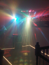 A dimly lit room with colorful disco lights. A table and railing are visible.