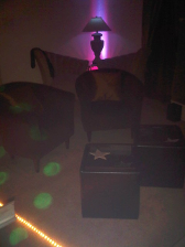 Cozy, dimly lit room with armchairs, a lamp casting pink and purple hues, and disco lights.