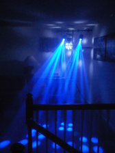 Blue stage lights illuminate a room, creating beams and shadows. Railing in the foreground.
