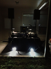 DJ setup outdoors at night with speakers, turntables, and spotlights.