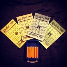 Four bingo cards in yellow and green with a blue container of orange markers on a black surface.