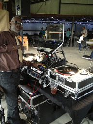 DJ at a party, wearing a brown shirt and tie, operating his turntables and mixer.