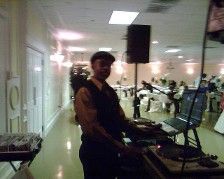 DJ at a wedding reception. Man in a cap, behind a laptop and turntables, smiling in a well-lit room.