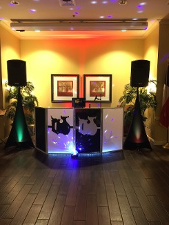 DJ setup with speakers, lights, and illuminated booth in a venue with artwork.
